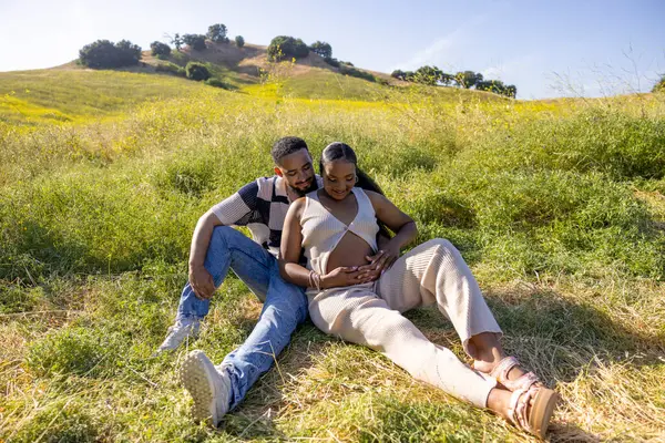 Afrikalı bir Amerikalı çift, hamileliklerini mutlu bir şekilde kutluyor. Sevgiyle kucaklıyor ve gelecekle ilgili duygusal bağlarını ve beklentilerini yansıtıyor.