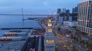 Alacakaranlıkta San Francisco 'nun muhteşem hava manzarası ikonik ufuk çizgisini ve geniş rıhtımı sergiliyor. Yumuşak bir sis bulutu güzel körfezi nazikçe sarıyor.