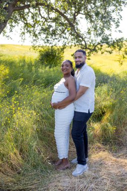 Sevgi dolu bir Afrikalı Amerikalı çift, sıcak yaz mevsiminin keyfini çıkarırken, koca, karısına şefkatle sarılıyor. Güzel bir bebek tümseği.