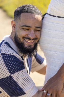 Afrika kökenli Amerikalı bir çift canlı bir yaz ortamında hamileliklerini neşeyle kucaklıyor. Ailelerinin yeni gelişi ve gelecekteki gelişimi için derin bağlantılarını ve heyecanlarını yansıtıyor.