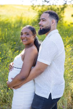 Gerçekten iç açıcı bir anda, güzel bir kucaklaşmayı paylaşan neşeli bir çifte tanık oluyoruz. Kocasının hamile karısını sevgiyle kucakladığına doğayla çevrili sakin bir ortamda.