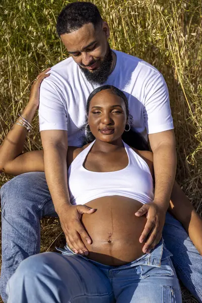 Sakin bir açık hava ortamında, neşeli hamile bir çift sıcak yaz güneşinin tadını çıkarıyor, doğaları gereği güzelliklerle çevrili bebeklerinin gelişini hevesle bekliyorlar.