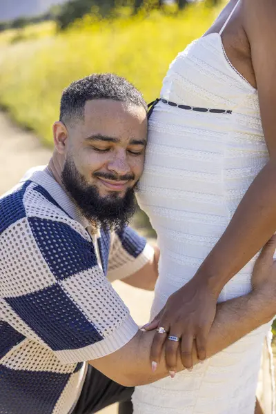 Sevgi dolu bir Afrikalı Amerikalı çift, mutlu bir şekilde dışarıda güzel bir yaz gününün tadını çıkarıyor. Onları çevreleyen huzurlu ve resmedilmiş doğal ortamda hamileliğin güzelliğini tamamen kucaklıyor.