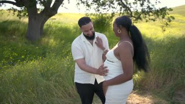Çarpıcı bir açık hava ortamında, neşeli bir Afrikalı Amerikalı çift hamileliklerini kutluyor, doğanın güzelliği içinde sevgi ve bağlantı yayarak, enfes yaz titreşimlerini kucaklıyor.