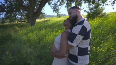 Afrika kökenli Amerikalı bir çift, yazları doğal ortamda güzelliği kucaklayarak, mutluluklarını artıran canlı yeşillikler ve sıcak güneş ışığıyla çevrelenmiş hamileliklerini kutluyor.