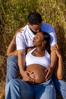 Son derece neşeli bir Afrikalı Amerikalı çift dışarıda güneşli, güzel bir günün keyfini çıkarıyor. Harika hamileliklerini sıcaklık, sevgi ve mutluluk duygusuyla kutluyorlar.