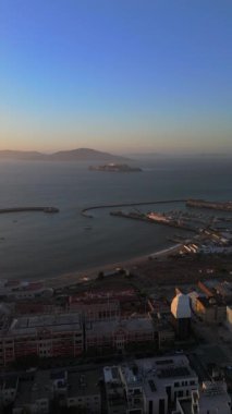 San Francisco marinası ve Alcatraz hapishanesi üzerindeki hava görüntüleri. Gün batımında denize açılacak tekneli sakin bir sahil şeridi. Seyahat için mükemmel.,