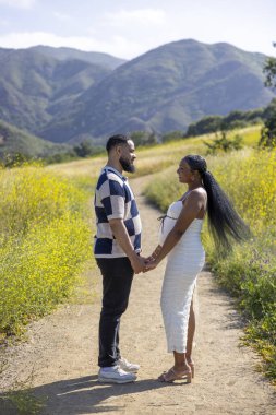 Neşeli ve beklenen bir çift açık havada, yemyeşil ve görkemli dağlarla çevrili, sevgi ve beklentiyle dolu ebeveynliğe doğru heyecanlı yolculuklarını kutluyorlar.