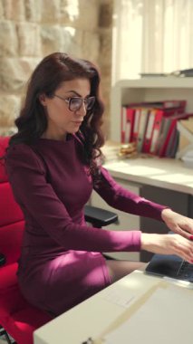 Modern bir ofiste, kararlı bir iş kadını laptopuyla çalışır, canlı çiçeklerle çevrili ve üretkenliğini, yaratıcılığını, hırsını arttıran zarif bir estetik ile.