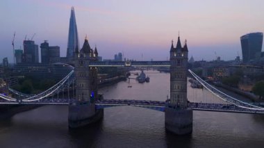 Bu hava görüntüsü, alacakaranlıkta aydınlanan Tower Köprüsü 'nü yakalıyor. Londra' nın canlı ufuk çizgisini ve Thames Nehri 'ni gösteriyor. Büyüleyici bir gece manzarası şehrin ikonik simgelerini ve cazibesini vurguluyor.