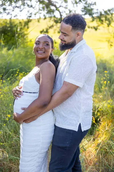 Sevgi dolu bir Afrikalı Amerikalı çift, yaz güneşinin altında hamileliklerinin heyecan verici haberini kutlarken dışarıda güzel ve neşeli bir anı paylaşıyor.