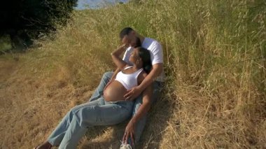 Afrika kökenli Amerikalı bir çift, sıcak bir yaz gününde neşeli bir şekilde birbirlerini kucaklıyor. Doğanın canlı güzelliği ve hayat dolu renkleri arasında geçirdikleri güzel hamileliklerini kutluyorlar.