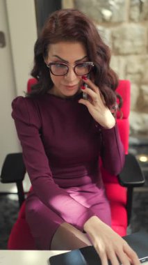 Zarif, mor bir elbise giymiş genç bir bayan profesyonel, parlak ve canlı bir ofis ortamında, çağdaş masasında çalışırken önemli bir telefon görüşmesi yapıyor.