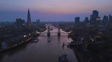 Bu çarpıcı hava manzarası, alacakaranlık zeminine karşı güzelce aydınlatılmış Tower Köprüsü 'nü yakalıyor. Londra' nın büyüleyici ufkunu ve Thames Nehri 'nin sarmal genişliğini vurguluyor.