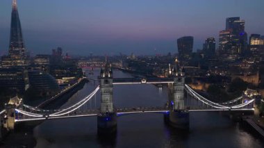 Bu hava aracı görüntüsü Tower Köprüsü 'nü ve Londra ufuk çizgisini yakalıyor, büyüleyici alacakaranlık atmosferini çerçeveliyor ve Thames Nehri' nin şehirde süzülen huzurlu güzelliğini vurguluyor.