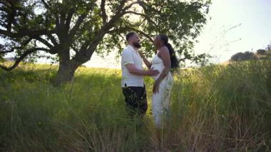 Neşeli bir çift, yakında ebeveyn olacak, güneşli bir yaz gününün tadını çıkarıyor, yeni bebeklerine olan sevgilerini ve beklentilerini kutluyor, huzurlu bir atmosferde bu özel anı kutluyorlar.