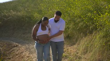 Sevgi dolu bir Afrikalı Amerikalı çift, yeşillik ve sıcaklıkla dolu büyüleyici doğal ortamda birlikte hamileliklerini kutlayarak keyifle dışarıda güneşli bir günün tadını çıkarıyor.