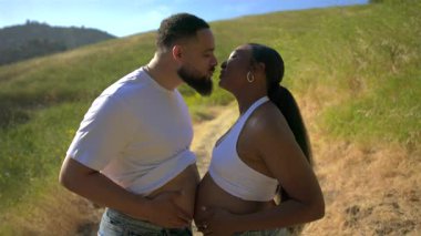 Güzel bir açık hava ortamında, sevgi dolu bir çift, hamileliklerini kutluyor ve yemyeşil ortamda ailelerinin geleceği hakkındaki derin bağlarını ve beklentilerini sergiliyor.