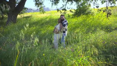 Neşeli bir Afrikalı Amerikalı çift, doğanın güzelliği içinde birbirlerini kucaklıyor. Parlak ve güneşli bir günde yemyeşil ile çevrili harika hamileliklerini kutluyorlar.