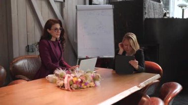 Modern bir ofiste, iki azimli kadın projelerini dizüstü bilgisayarlar ve tabletler kullanarak, işbirliği, takım çalışması ve yenilikleri teşvik ederek, işyerlerindeki genel yaratıcılığı artırarak tartışırlar.