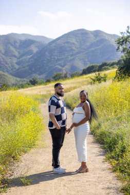 Neşeli bir Afrikalı Amerikalı çift, yazın sıcacık güzelliğini kucaklıyor. Hamileliklerini ve aşklarını huzur verici arka planda kutluyorlar.