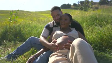 Afrika kökenli Amerikalı bir çift, hamileliği gülümseme ve samimi dokunuşlarla kutluyor, yazın sıcaklığının tadını çıkarıyor, ki bu da onların bu özel zamanlarda olan bağlarını derinleştiriyor.