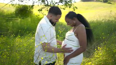 Çarpıcı derecede güzel bir Afro-Amerikan çifti dışarıda neşeli bir anı paylaşıyor. Gün ışığıyla dolu huzurlu ve huzurlu bir yaz ayının ortasında hamileliğin inanılmaz neşesini kutluyorlar.