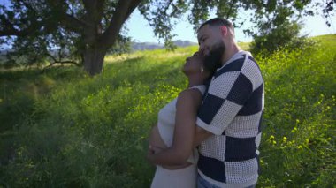 Afrika kökenli Amerikalı bir çift, hamileliklerinin heyecanlı yolculuğunu sevinçle kutlarken, yeşilliğin çarpıcı güzelliğiyle çevrelenmiş bir şekilde, açık havada tatlı ve hassas bir anın tadını çıkarıyor.