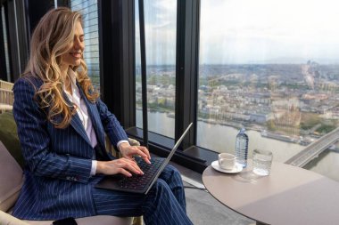 Şık ince çizgili takım elbiseli yetenekli profesyonel bir kadın laptopuna odaklanıyor, gökdelen ofisinden canlı bir şehir manzarasının keyfini çıkarıyor, üretkenlik ve hırs atmosferini teşvik ediyor.