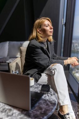 Kararlı ve kararlı bir iş kadını, profesyonel kariyer hedeflerine ulaşma hırsını ve sarsılmaz bağlılığını somutlaştıran, yüksek bir ofis penceresinden düşünceli bir şekilde bakar.