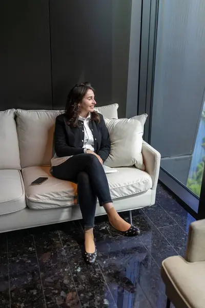 Modern bir ofiste, kendine güvenen bir iş kadını şık bir kanepede rahatlar, profesyonelliği ve sofistikeliği somutlaştırırken atmosferi aydınlatan pozitif enerji yayar.