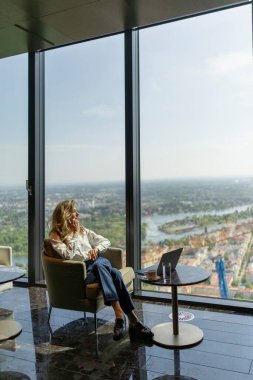 Şık ve çağdaş ofisinde, azimli bir iş kadını hak ettiği molayı alıyor, buharlı bir fincan kahvenin tadını çıkarırken geniş pencerelerinden canlı şehir manzarasına hayran kalıyor.
