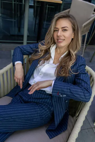 Şık ve modaya uygun çizgili bir takım elbise giymiş dengeli ve cilalı bir iş kadını açık havada rahatlatıcı bir andan zevk alıyor, özgüven ve profesyonellik havası yayıyor.