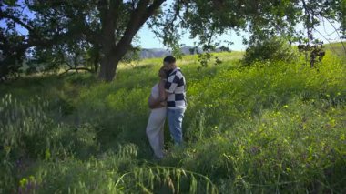 Canlı ağaçlar ve çiçeklerle dolu yemyeşil bir arazide, sevgi dolu bir çift, yakın ilişkilerinde sevgi ve sıcaklıkla hamileliklerini kutlayan hassas bir anı paylaşıyor.