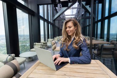 Modern bir ofiste, odaklanmış profesyonel bir kadın yüksek performanslı dizüstü bilgisayarı, zarif dekorları ve yüksek gökdelenleri olan hareketli bir şehir silueti manzarası ile dikkatle çalışır.