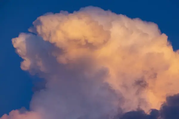 Gün batımının canlı renkleriyle güzelce aydınlatılan muhteşem bulut oluşumunun nefes kesici görüntüsü, gökyüzünün derin mavi tuvaline karşı inanılmaz sanatsal özellikler sergiliyor.