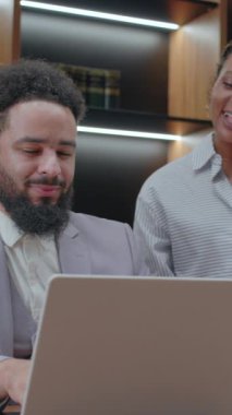 Modern bir ofiste, kendini işine adamış bir işadamı laptopun etrafında bir meslektaşıyla işbirliği yaparak, etkin takım çalışmalarını ve dinamik bir çalışma alanında proje hedeflerine ulaşma kararlılığını sergiliyor.