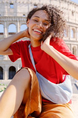 Neşeli genç bir kadın, Roma 'daki ikonik antik kolezyuma parlak, ışıl ışıl bir gülümseme ile poz veriyor. Gezinin ve çeşitli kültürlerin zenginleştiren güzelliğini güzel bir şekilde sergiliyor.