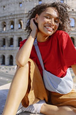 Neşeli ve hayat dolu genç bir kadın, görkemli Colosseum tarafından neşeli bir şekilde poz verdirirken, Roma 'nın büyüleyici güzelliğini zengin kültürüyle birlikte yansıtıyor.