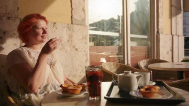 Güneşli bir kafede otururken çay ve hamur işlerinin tadını çıkaran bir kadın sahnesi. Yaşam tarzı ve mutfak temaları için mükemmel.