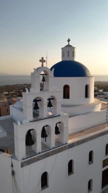 Santorini 'de mavi bir kubbe bulunan geleneksel bir Yunan kilisesinin nefes kesici bir günbatımına karşı olağanüstü bir mimari sergiliyor ve büyüleyici bir atmosfer yaratıyor.