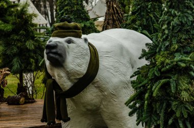 Kışlık şapkalı ve eşarplı bir kutup ayısı heykeli köknar ağaçları arasında harika bir fotoğraf mekanıdır.