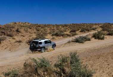 Tozlu Çöl Patikası 'nda Parlak Mavi Gök Macerası Sahnesi Altında Çalılarla Gezen SUV.