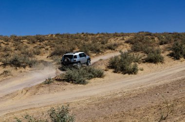 Tozlu Çöl Patikası 'nda Parlak Mavi Gök Macerası Sahnesi Altında Çalılarla Gezen SUV.