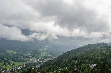 Dramatik bulutlu gökyüzü altında orman, kar ve bulutlarla dolu manzaralı dağlık dağ manzarası.
