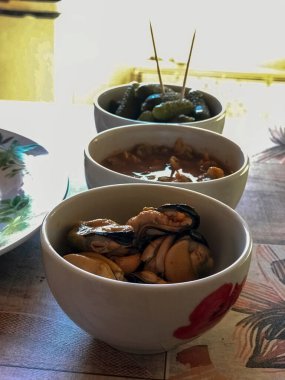 small ceramic bowls with mussels, cockles and gherkins in them