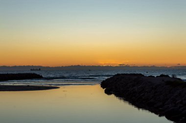 image of the sea at dawn next to the breakwaters where the river flows into the sea.