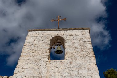 Arka planda mavi gökyüzüne karşı duran beyaz duvarlı bir inziva yerinin çan kulesinin görüntüsü.