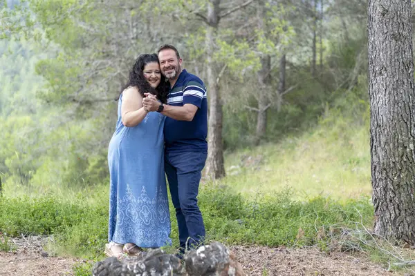 Bir adam ve bir kadın tarlada duruyor, gülümsüyor ve el ele tutuşuyorlar. Sahne mutlu ve romantik.