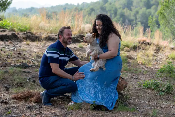 Bir adam ve bir kadın ormanda bir köpekle birlikte bir kütükte oturuyorlar. Adam çizgili bir gömlek ve kot pantolon giyiyor. Kadın mavi bir elbise giyiyor. Sahne huzurlu ve rahat.